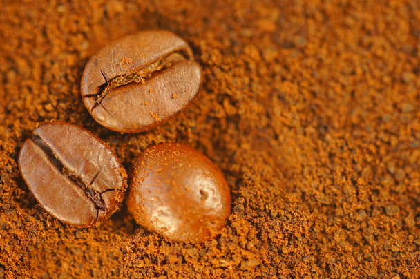 Koffie - koffiebonen op gemalen koffie. Grote close-up van de boon. Bruine, warme kleuren van het beeld. Gedroogde koffie onder de bonen. - Foto, afbeelding