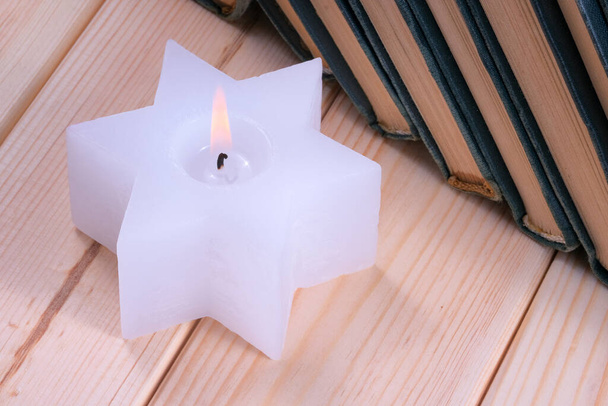 Egy hatágú zsidó csillag alakú fehér paraffin gyertya áll egy halom zöld kötésű könyv mellett egy fa asztalon. - Fotó, kép