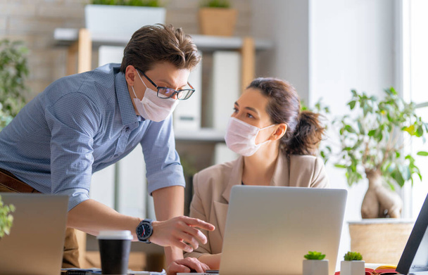 Businessman and businesswoman with medical mask working in office. Covid-19 time. - Zdjęcie, obraz