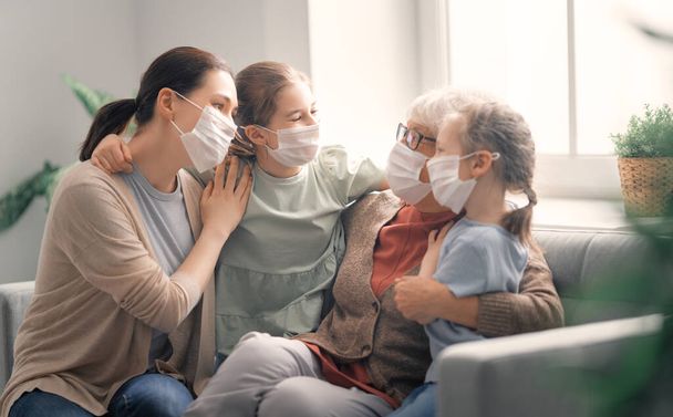 A nice girls, her mother and grandmother enjoying spending time together at home. People wearing face masks. - Valokuva, kuva