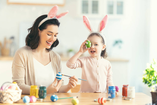 Happy holiday! A mother and her daughter are painting eggs. Family preparing for Easter. Cute little child girl is wearing bunny ears. - Valokuva, kuva
