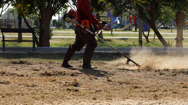 Dělníci odstraňují trávu sekačkou na trávu. Tvrdě pracující muži tahali trávu na zemi malým motorem a způsobovali, že se trosky a tráva šířily s kopírkou. Selektivní zaměření - Fotografie, Obrázek