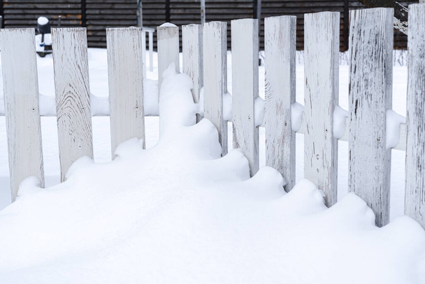 Biały zabytkowy drewniany płot nad środkiem pokryty śniegiem w zimie - Zdjęcie, obraz