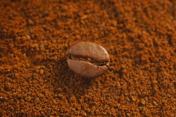 Grano de café tostado - puesto sobre el café molido usado. Primer plano en grano de café con fondo borroso. Color marrón, muchos detalles visibles. - Foto, imagen