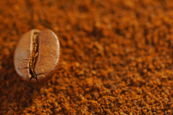 Geröstete Kaffeebohnen - über gebrauchten gemahlenen Kaffee gelegt. Nahaufnahme von Kaffeebohnen mit verschwommenem Hintergrund. Braune Farbe, viele sichtbare Details. - Foto, Bild
