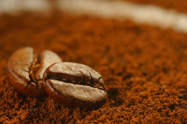 Geroosterde koffieboon - gelegd over gebruikte gemalen koffie. Close-up van koffieboon met wazige achtergrond. Bruine kleur, veel zichtbare details. - Foto, afbeelding