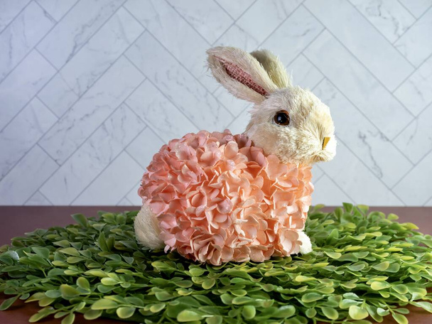 Decoración de conejo de Pascua sentado sobre hojas verdes, cubierto de flores de melocotón, perfecto para las vacaciones de primavera! - Foto, imagen