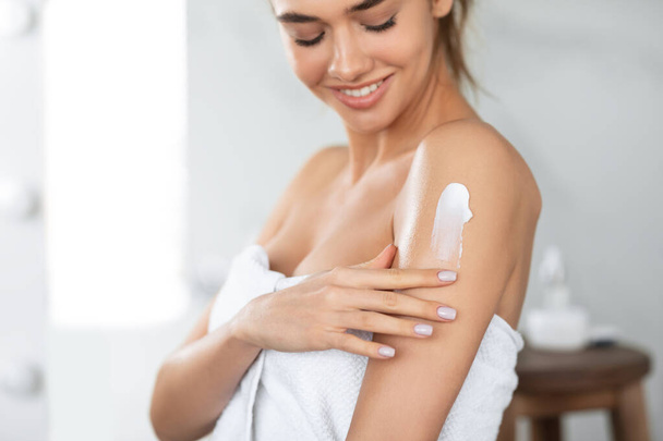 Жінка застосовує зволожуючий лосьйон на плечах догляд за шкірою в приміщенні
 - Фото, зображення