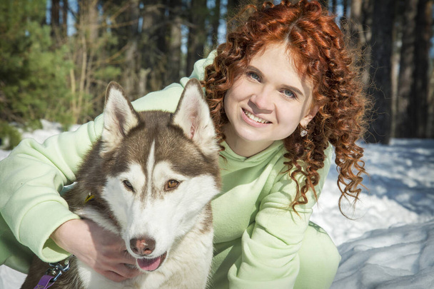 Im Winter, an einem sonnigen Tag im Wald, umarmt ein Mädchen einen Husky-Hund. - Foto, Bild