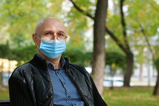 Bald senior man in medical protective mask and glases looks at the camera. Covid concept health and safety, coronavirus quarantine, next wave covid virus protection - Photo, Image