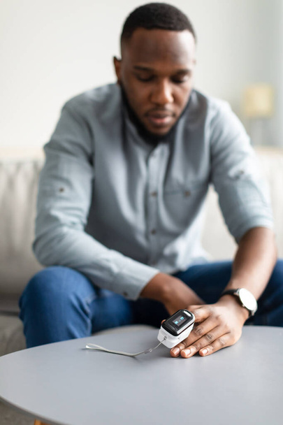 Homem negro medindo o nível de saturação de oxigênio com oxímetro de pulso no interior - Foto, Imagem