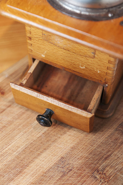 Vista parcial de molinillo de café de madera manual con cajón abierto en piso de madera desgastado.  - Foto, imagen
