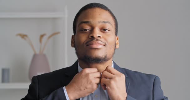 Retrato de afroamericano confiado hombre de negocios elegante novio chico étnico preparándose para la reunión de boda en la oficina lleva traje negro elegante caro y camisa azul botón cuello mirando a la cámara - Metraje, vídeo