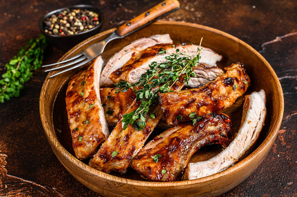 Cut BBQ grilled pork rack spareribs in a wooden plate. Dark background. Top view. - Photo, Image