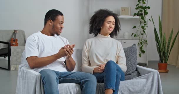 Afro-americano casal recém-casados namorado e namorada sentado em casa sofá brigando jurar ciumento marido gritando mulher cobrindo orelhas com dedos exige silêncio faz gesto mão proibida - Filmagem, Vídeo