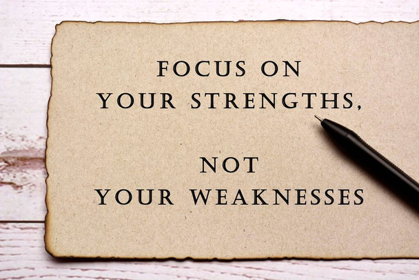 Motivatív és inspiráló idézetet égetett szélű barna papír tollal a fa íróasztalon - Fókuszálj az erősségekre, ne a gyengeségeidre - Fotó, kép