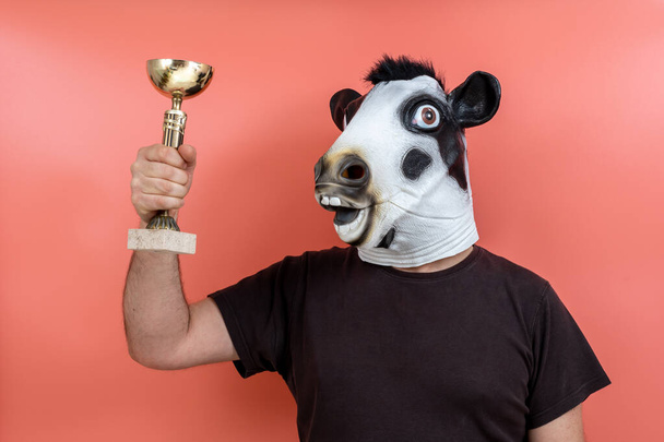 persona in costume con maschera di mucca che mostra trofeo su sfondo rosa - Foto, immagini