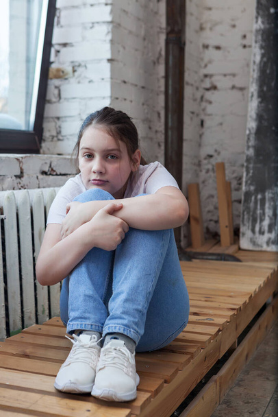 Tyttö pre-teini-ikäinen surullinen lähellä ikkunaa, halaamalla polviaan   - Valokuva, kuva