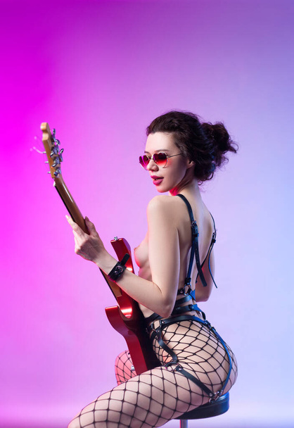 γυμνή γυναίκα σε bdsm λουρί με κιθάρα σε νέον φως - Φωτογραφία, εικόνα