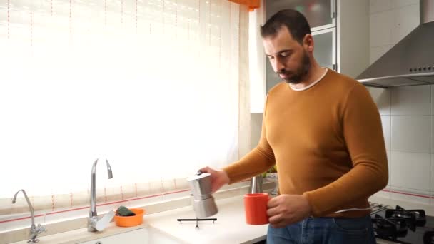 Een man met een baard in een oranje trui die zichzelf een kop hete koffie inschenkt. Beginbegrip - Video