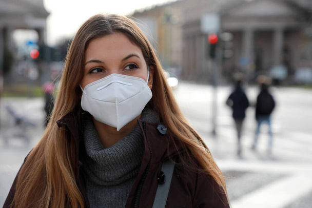 Sense of bewilderment. Close up of young woman in winter clothes walking in street wearing protective mask FFP2 KN95. Girl with face mask feeling alone during a pandemic. - Photo, Image