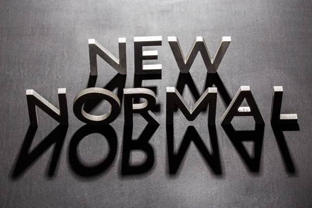 new normal word composed of silver metal letters on a flat matt black surface with shadows backlit - Photo, Image
