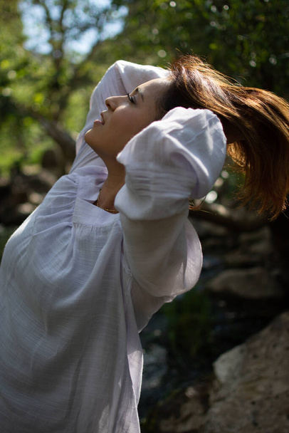 Латиноамериканка откидывает волосы на солнце перед лесом, а весной в тени течет ручей. - Фото, изображение