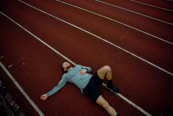 Caucasian male athlete lying down on tracking field - Фото, изображение