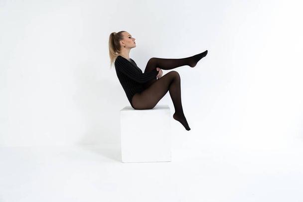 Modell in schwarzen Strumpfhosen auf weißem Hintergrund. Akrobatisch tanzende Frau posiert. heiße blonde Mädchen mit langen Beinen in Dessous - Foto, Bild