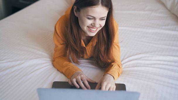 かなり明るい女性がノートパソコンのインターネットの前のベッドに横たわっています - 写真・画像