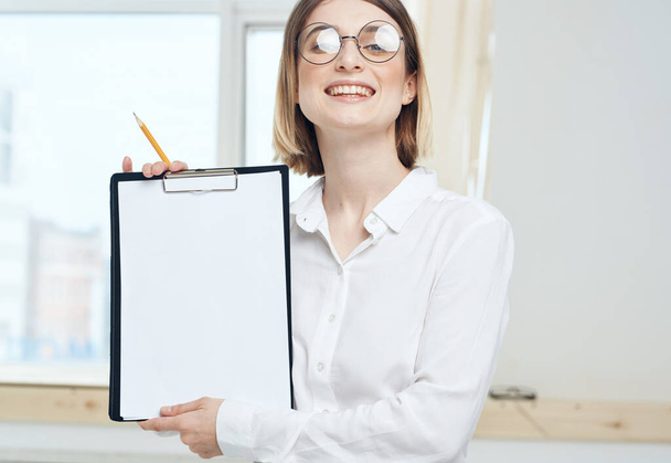 Eine Frau hält einen Ordner mit einem weißen Blatt Papier und einem Fenster im Hintergrund - Foto, Bild