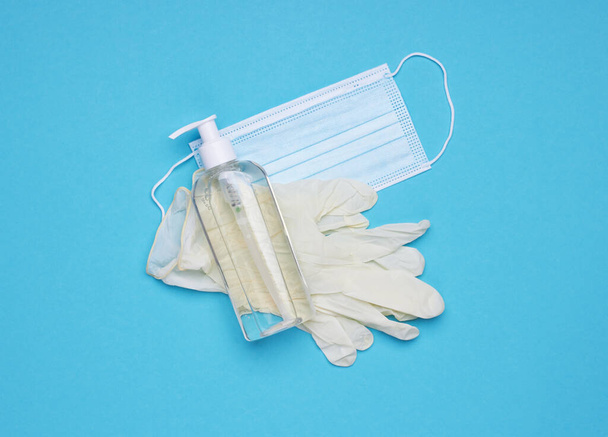 Gezichtsmasker, handreiniger fles en latex handschoenen. Coronavirus preventie medisch chirurgisch masker met de hand ontsmettingsgel, hand hygiëne coronavirus bescherming. Op een blauwe achtergrond. - Foto, afbeelding