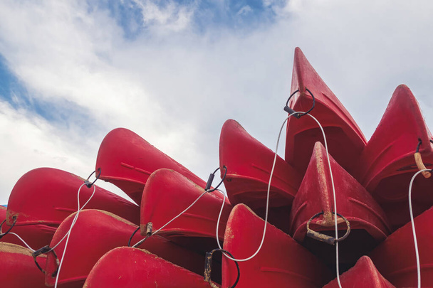 group of red kayaks piled up against each other on the shore seen from below with a blue sky in the background - Photo, Image