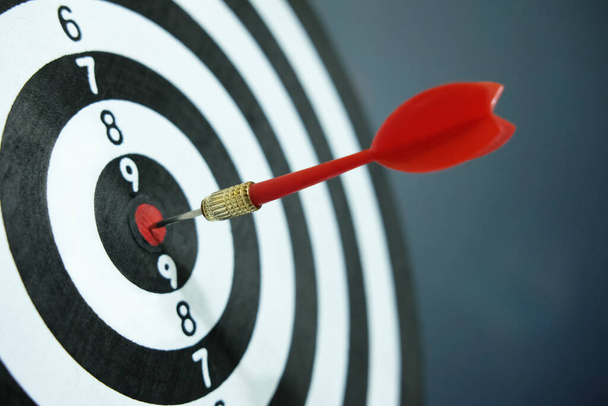 Foto conceptual de la estrategia de negocio / precisión - una flecha roja que se pega directamente en el centro del tablero de dardos objetivo - Foto, imagen