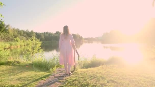 Giovane donna bionda che indossa occhiali passeggiando lungo il lago al tramonto in una sera d'estate, 4k - Filmati, video