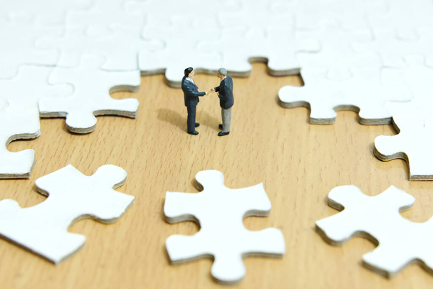 Business strategy conceptual photo - Miniature businessman make handshake partnership in the center of jigsaw puzzle piece - Foto, Imagen