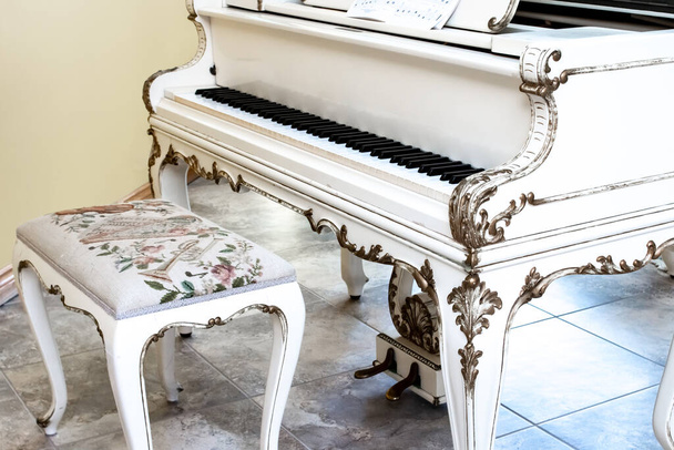 Un beau piano à queue de bébé blanc avec des clés en ivoire et un banc rembourré orné sur tuile beige. Home interior, Londres, Canada. Plan d'angle. - Photo, image
