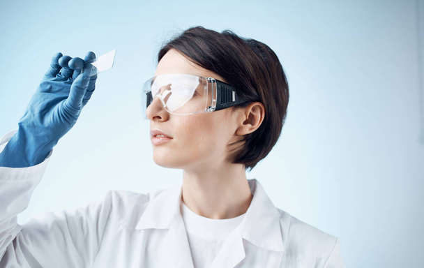 Tıbbi eldivenli kadın laboratuvar asistanı mikroskoptan camlara bakıyor. - Fotoğraf, Görsel