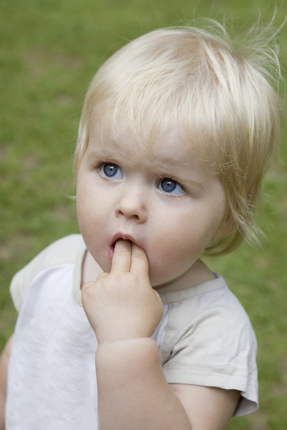 Portrait of little cute blond serious baby girl. Her fingers in mouth - Fotó, kép