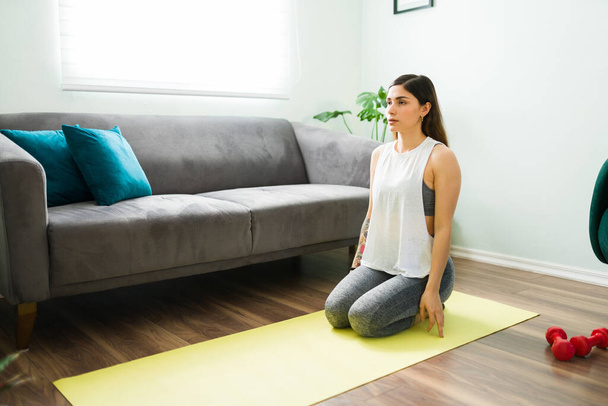 Aktywna młoda kobieta siedząca w pozycji grzmotu na macie do jogi. Latynoska ćwiczy i wykonuje ćwiczenia oddechowe w salonie - Zdjęcie, obraz