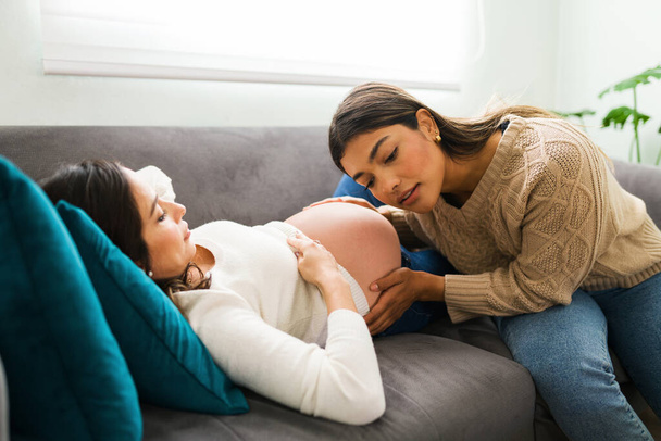 Houkutteleva kätilö tai doula laittaa korvansa lähelle valkoihoisen raskaana olevan naisen paljasta vatsaa kuuntelemaan vauvan sykettä.  - Valokuva, kuva