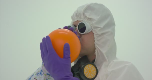 El hombre con un traje de protección química infla un globo naranja, cámara lenta - Metraje, vídeo