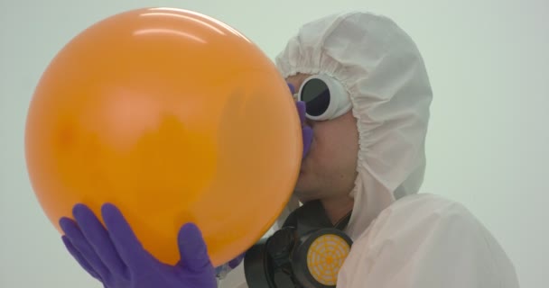 El hombre con un traje de protección química infla un globo naranja, cámara lenta - Metraje, vídeo