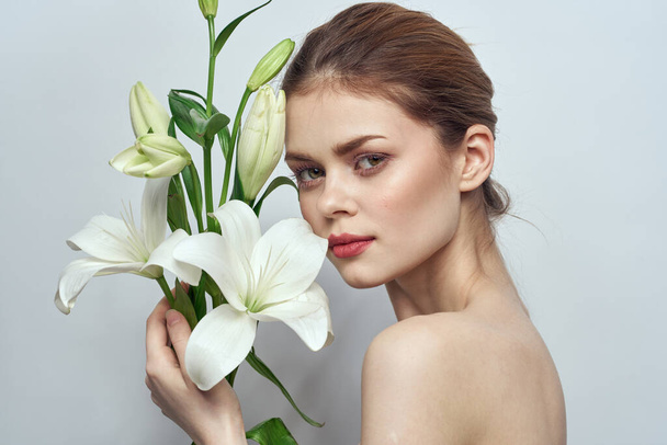 Beautiful girl with a bouquet of white flowers on a light background naked shoulders clean skin spring - Foto, imagen