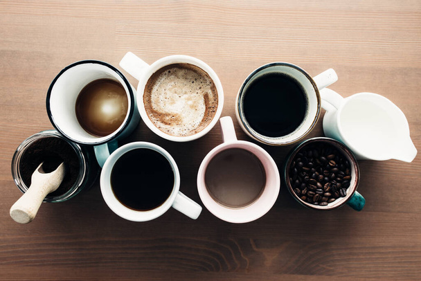 Useita kahvikuppeja, maitoa, papuja ja jauhettua kahvia purkissa puupohjalla. Laadukas kuva - Valokuva, kuva