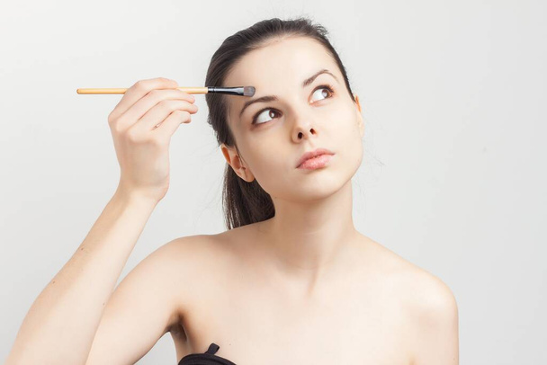 donna con spalle nude che applica la spazzola per il trucco sulla procedura viso - Foto, immagini