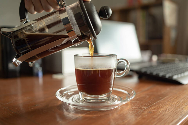 наливать кофе из французского пресса в чашку на рабочем столе дома - Фото, изображение
