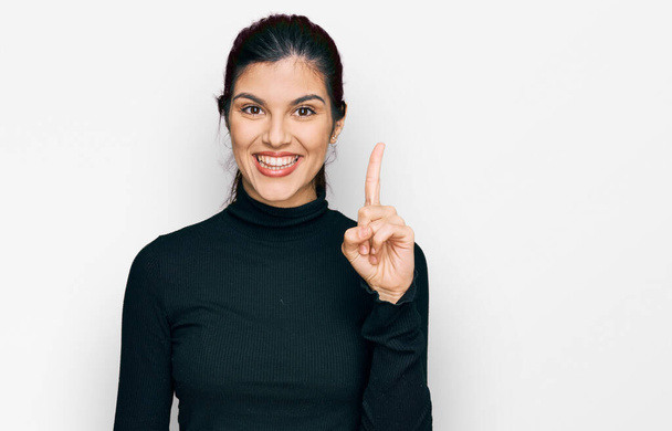 Jeune femme hispanique portant des vêtements décontractés montrant et pointant du doigt numéro un tout en souriant confiant et heureux.  - Photo, image