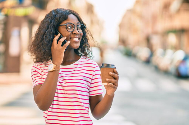 Giovane ragazza afroamericana che parla sullo smartphone bevendo caffè in città. - Foto, immagini