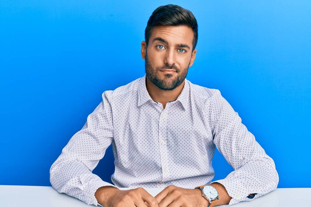 Handsome hispanic man wearing business clothes sitting on the table looking sleepy and tired, exhausted for fatigue and hangover, lazy eyes in the morning.  - Foto, imagen